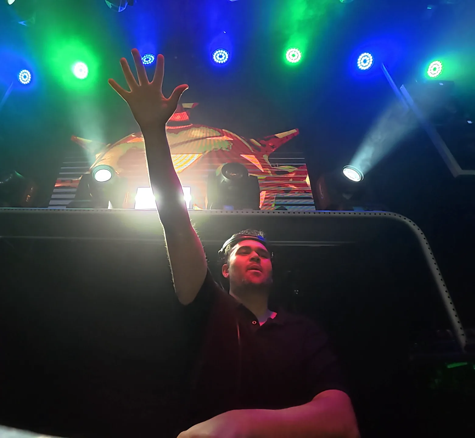 IWARO raising his hand beneath blue and green stage lights
